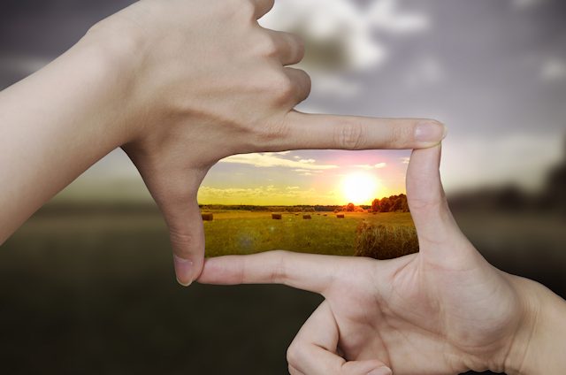 Hände rahmen eine Landschaft im Sonnenuntergang ein